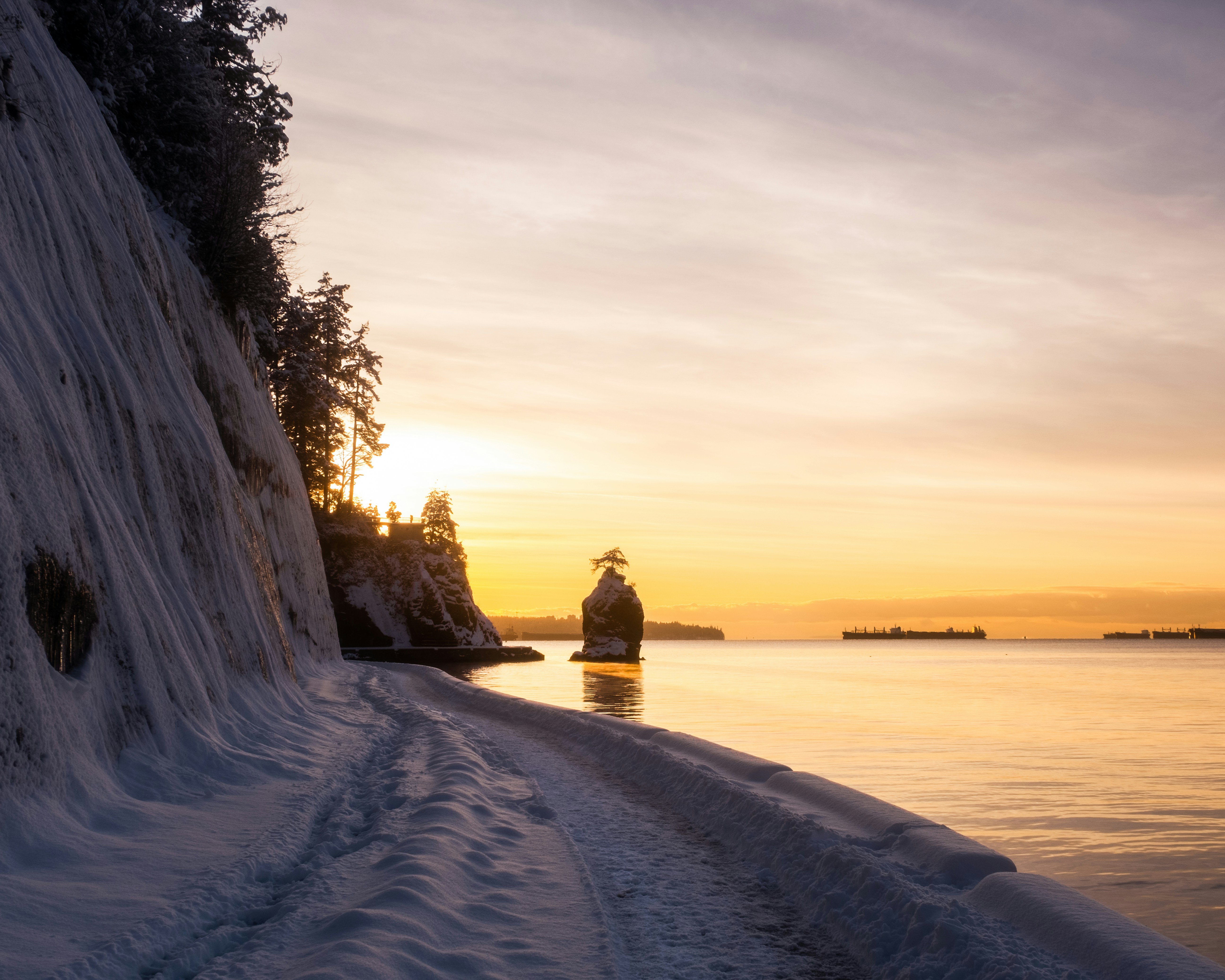 a person standing on a snow covered beach next to a body of water