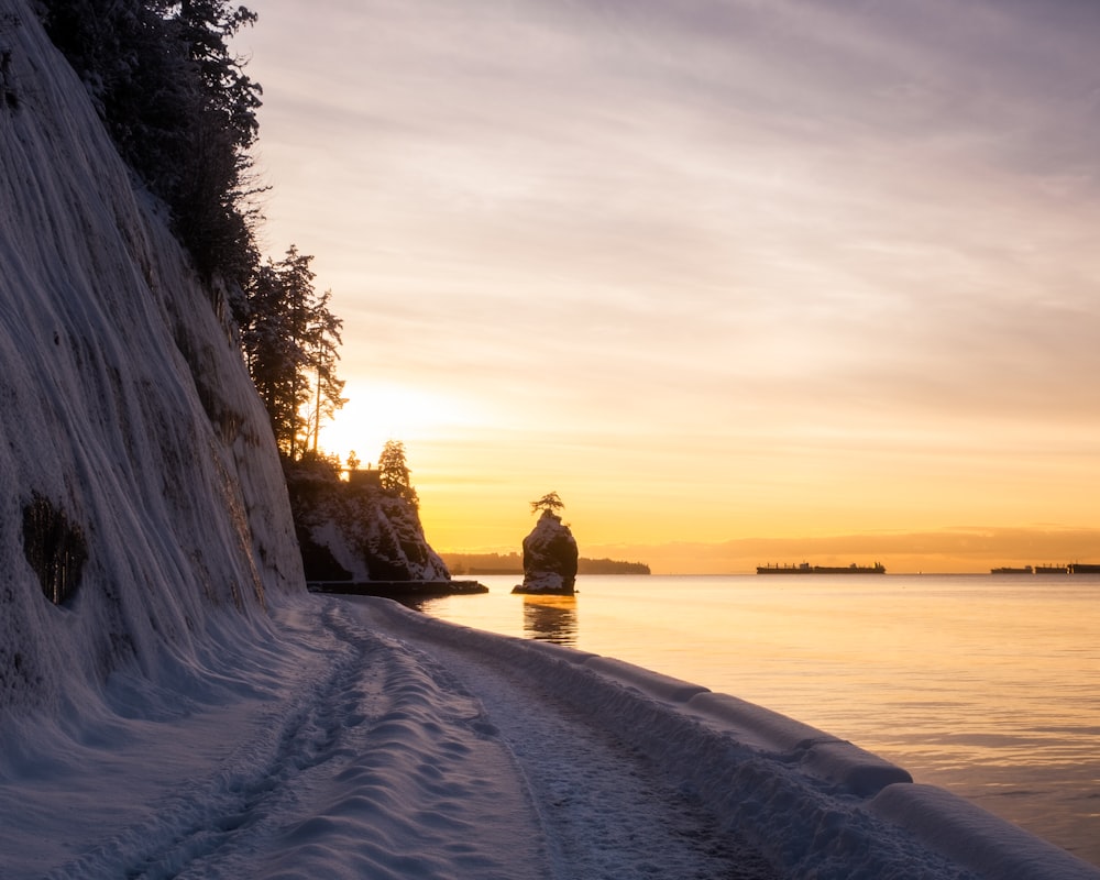 a person standing on a snow covered beach next to a body of water