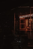A cozy and dimly lit outdoor food stall with warm string lights hanging above. The stall has a menu board and several signs promoting items such as authentic Cornish pasties. The atmosphere suggests a welcoming and rustic setting.
