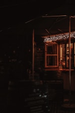A cozy and dimly lit outdoor food stall with warm string lights hanging above. The stall has a menu board and several signs promoting items such as authentic Cornish pasties. The atmosphere suggests a welcoming and rustic setting.