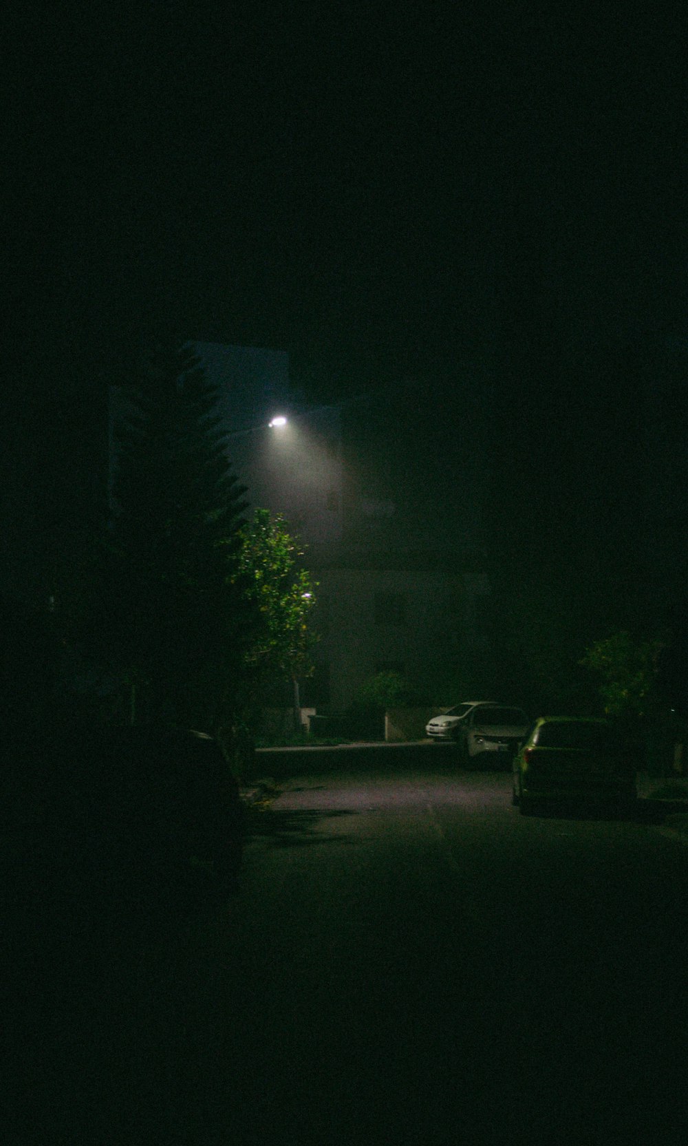 a dark street at night with cars parked on the side of the road