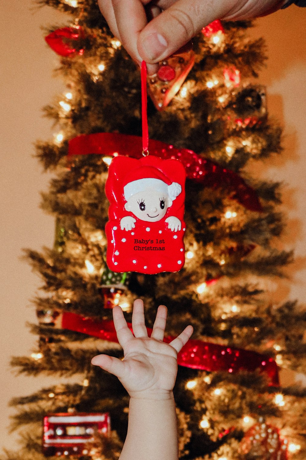 Una mano che tiene un ornamento natalizio davanti a un albero di Natale