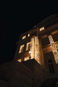 A beautifully lit commercial building at dusk showcasing elegant white and champagne gold holiday lights along the roofline and palm trees.