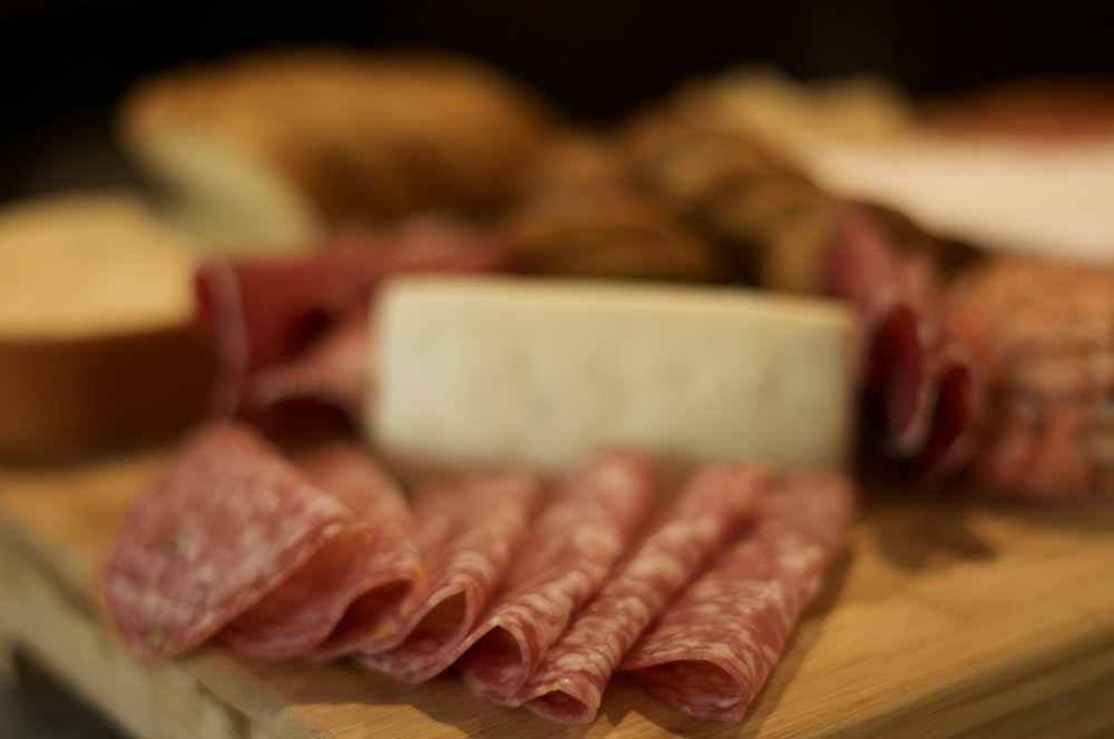 a wooden cutting board topped with meat and cheese