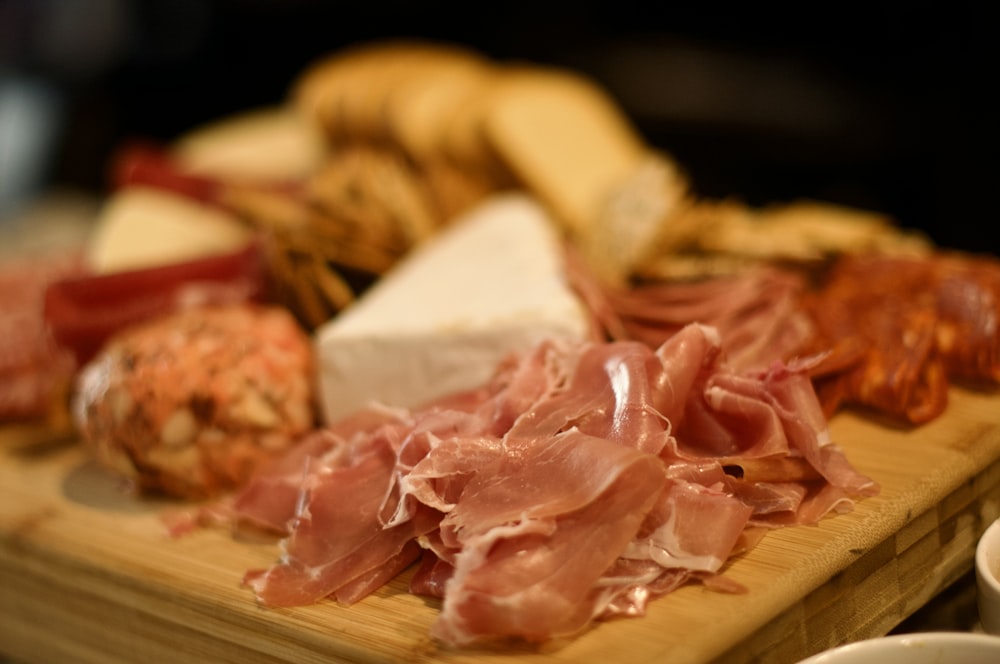 a wooden cutting board topped with meat and cheese