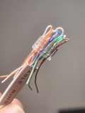 A close-up view of a bundle of untwisted electronic wires, each with different colors, held together by a transparent connector. The wires include orange, blue, green, and brown colors among others. A label marked with 'CABLE ROHS' is attached to the wire bundle.