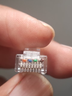 A close-up of a hand holding a transparent RJ45 Ethernet connector, displaying colored wires inside.