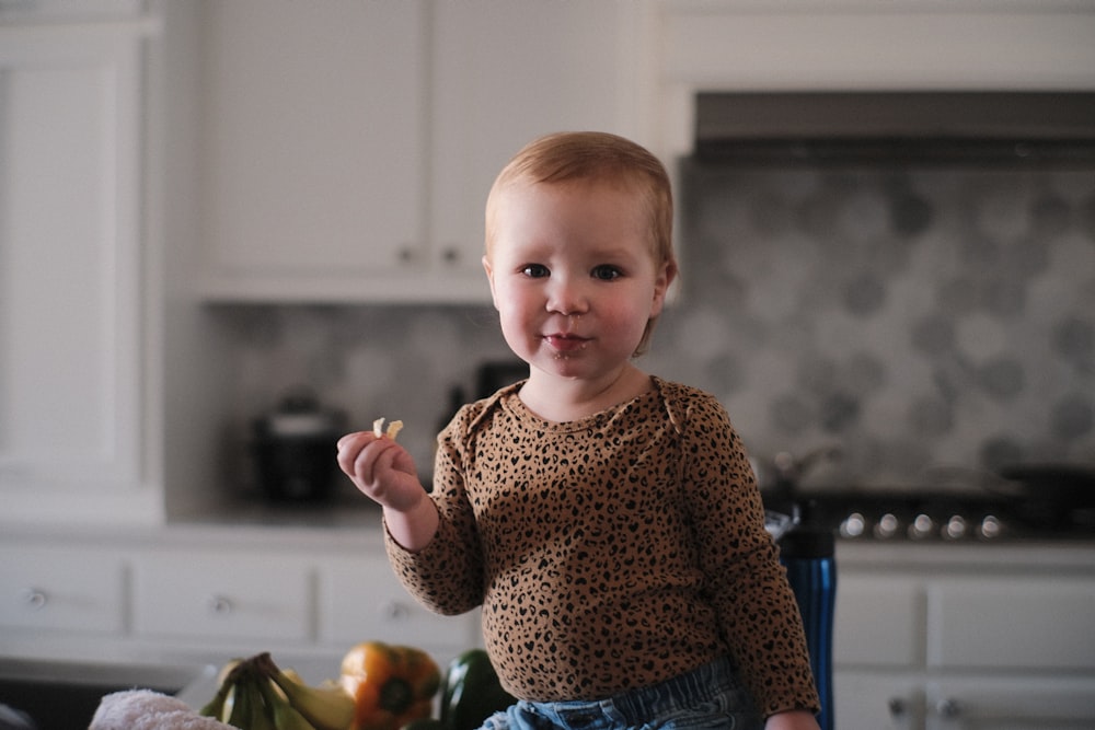 a little girl standing in a kitchen holding a piece of food
