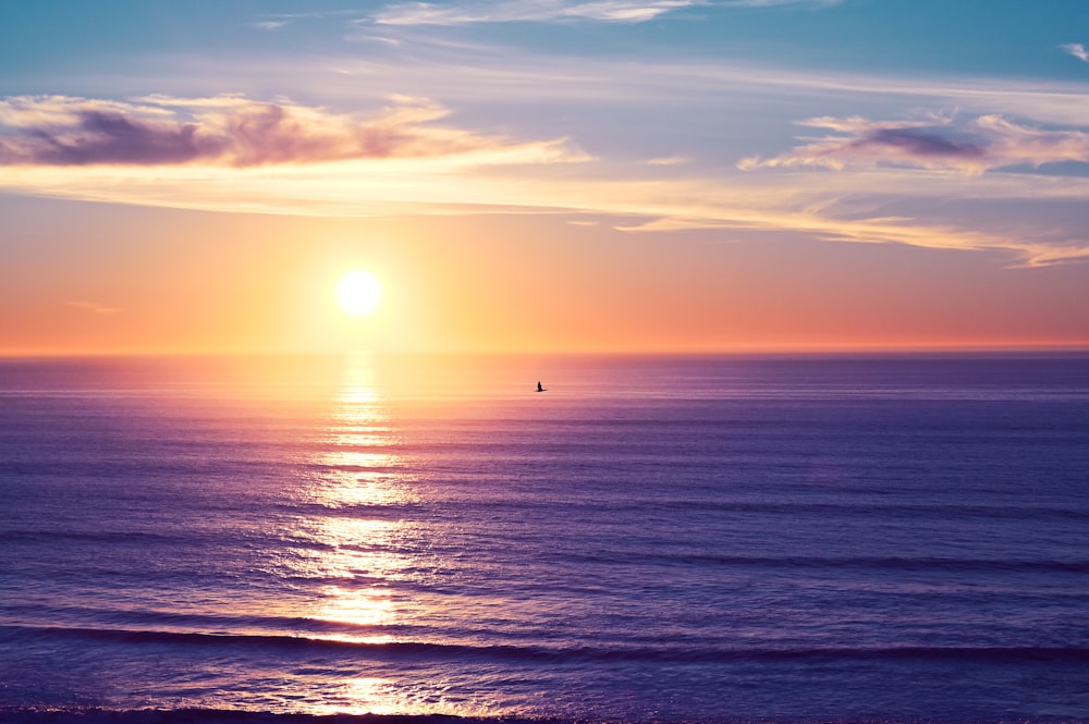 the sun is setting over the ocean with a sailboat in the distance
