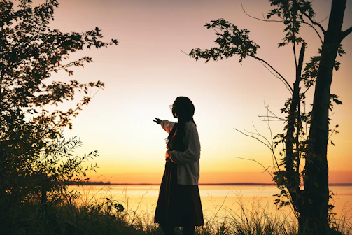 A scenic outdoor shot featuring Ahmad Raza standing thoughtfully by a lake at sunset