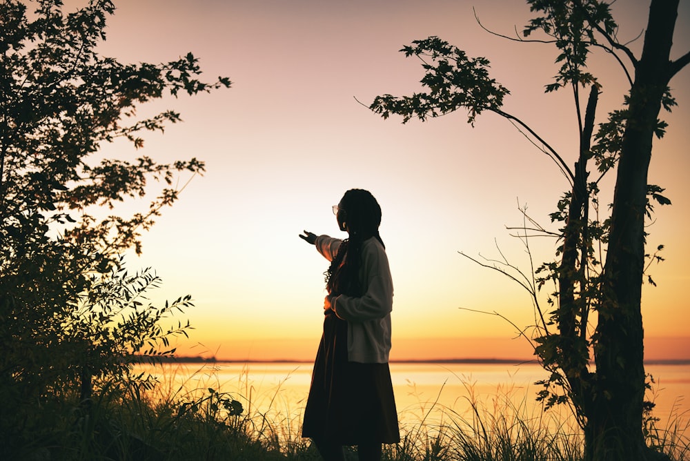 a woman standing in front of a lake at sunset