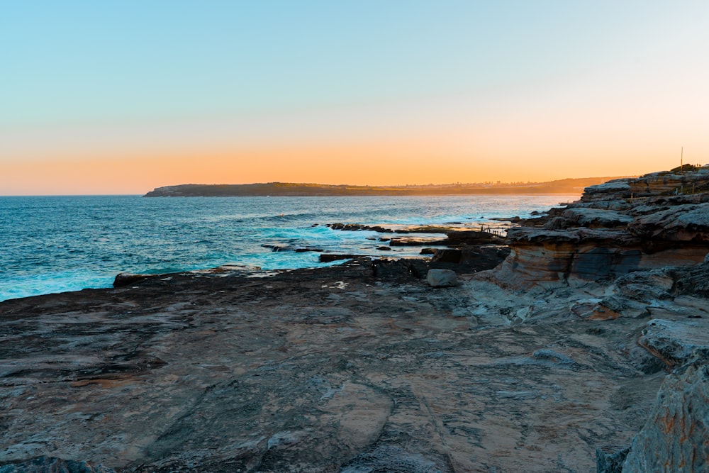 the sun is setting over the ocean on the rocky shore