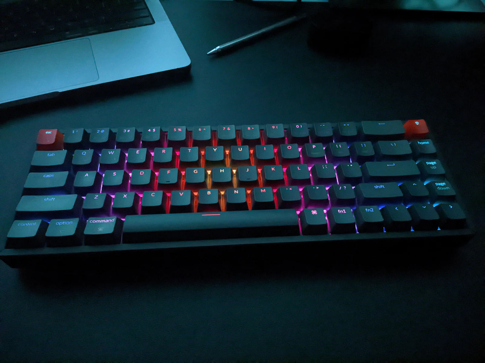 A dark desk with a laptop and RGB mechanical keyboard
