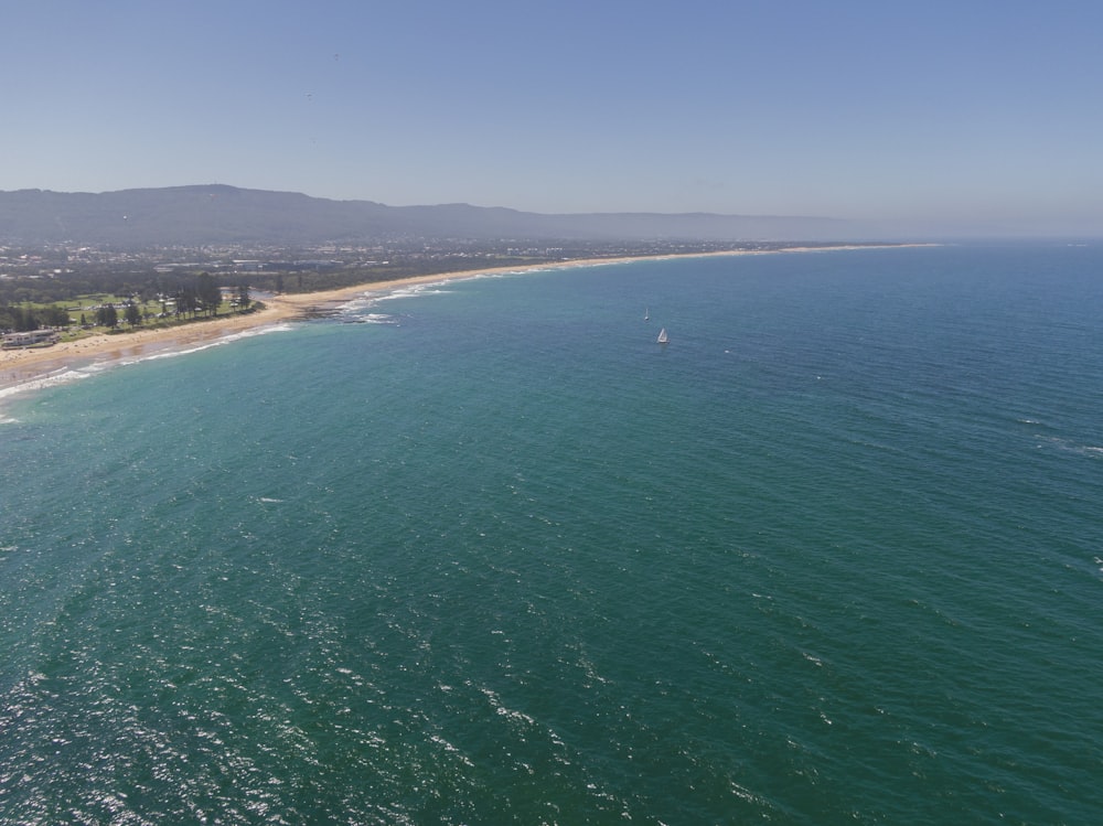 an aerial view of a beach with a sailboat in the water