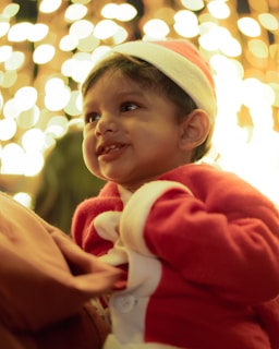 Close-up of a smiling child wearing a Santa hat with twinkling lights background