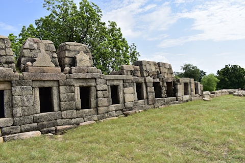 a stone wall in a grassy area with trees in the background
