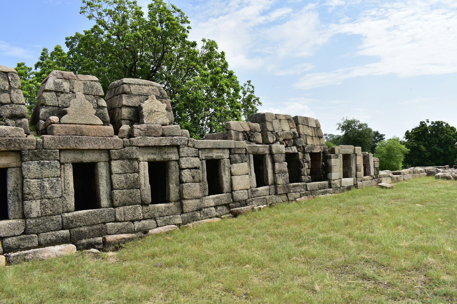 a stone wall in a grassy area with trees in the background