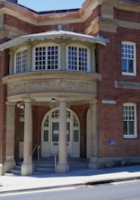 An entrance to a brick building with a rounded portico labeled 'Children's Court'. The structure features tall columns and an arched doorway with glass panes. A sign reading 'Albion St' is visible, along with a wheelchair accessibility symbol.