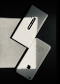 Two white smartphones are laid on a dark surface, intersecting at an angle. One smartphone is a Nokia model with the back camera and model name visible, while the other is an iPhone with the Apple logo and other inscriptions readable. The image has a high contrast with shadow and light creating a striking play.