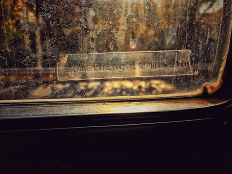 A worn-out vintage window with a label reading 'something is missing.' The glass is dusty and scratched, and there are tree branches faintly visible outside.