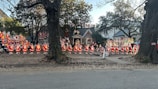 Numerous Santa Claus figures are arranged in a front yard with some additional holiday characters. They are placed in front of a house surrounded by trees, enhancing the festive holiday atmosphere.