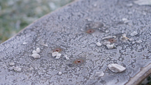 Close-up of dry ice pellets blasting a rusty engine part, with frost forming around the impact area.