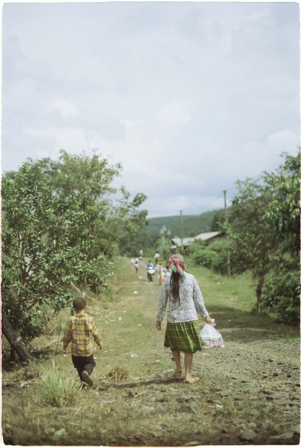 a woman and child walking down a dirt road