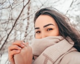 A model wrapped in a scarf styled as a shawl, standing against a snowy backdrop with gentle wind.