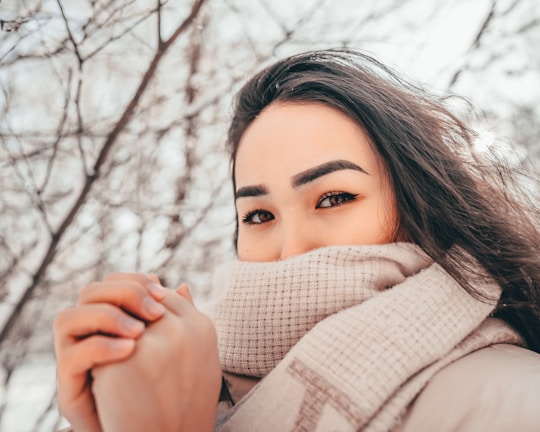 A model wrapped in a scarf styled as a shawl, standing against a snowy backdrop with gentle wind.