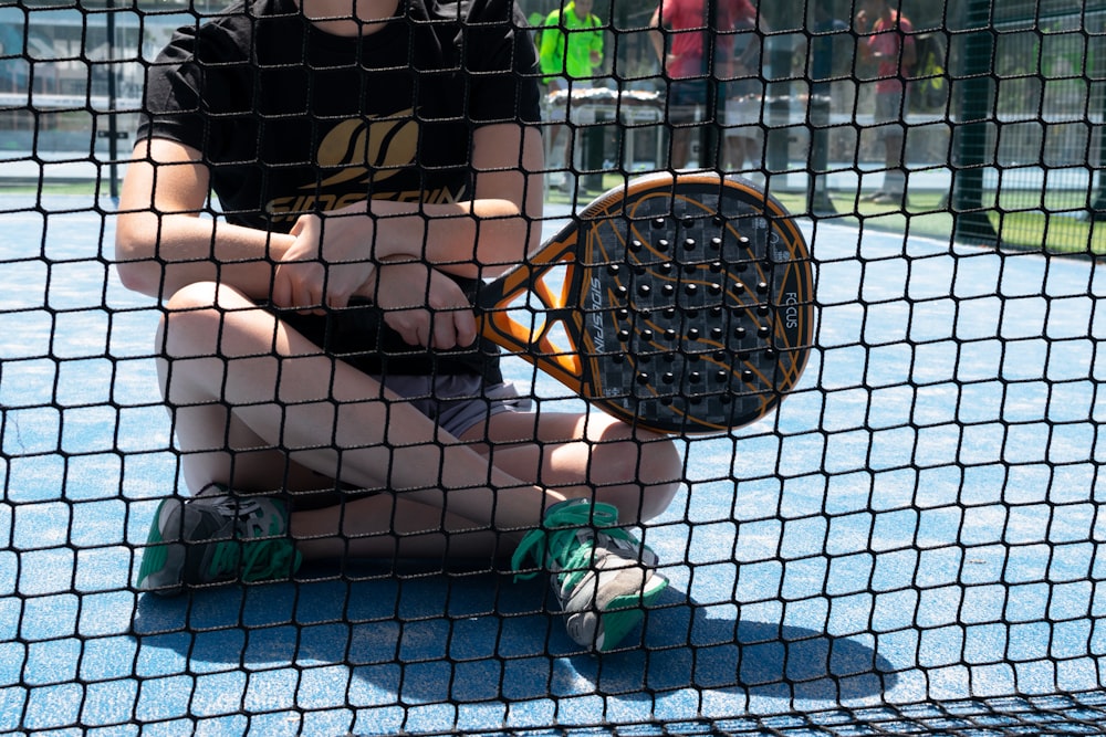 a young boy sitting on the ground holding a tennis racket