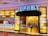 A vibrant entrance to a buffet restaurant featuring a bold sign with the word 'BUFFET' illuminated. The walls are decorated with a mosaic of colorful panels, predominantly in shades of yellow and orange. The interior is visible through the open entrance, showing a warmly lit hallway with decorative light fixtures. Signs on the wall highlight various food options such as rotisserie and seafood market.