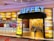A vibrant entrance to a buffet restaurant featuring a bold sign with the word 'BUFFET' illuminated. The walls are decorated with a mosaic of colorful panels, predominantly in shades of yellow and orange. The interior is visible through the open entrance, showing a warmly lit hallway with decorative light fixtures. Signs on the wall highlight various food options such as rotisserie and seafood market.