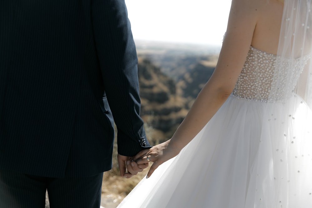 a bride and groom hold hands as they stand on top of a mountain