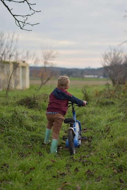 a young boy riding a blue bike on a lush green field