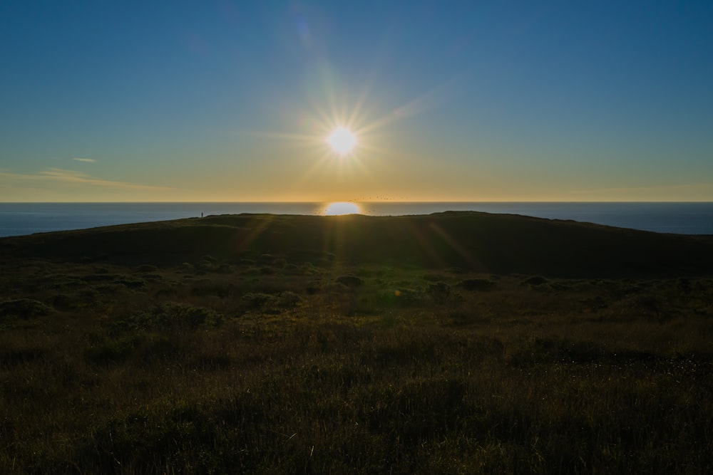 the sun is setting over a grassy hill