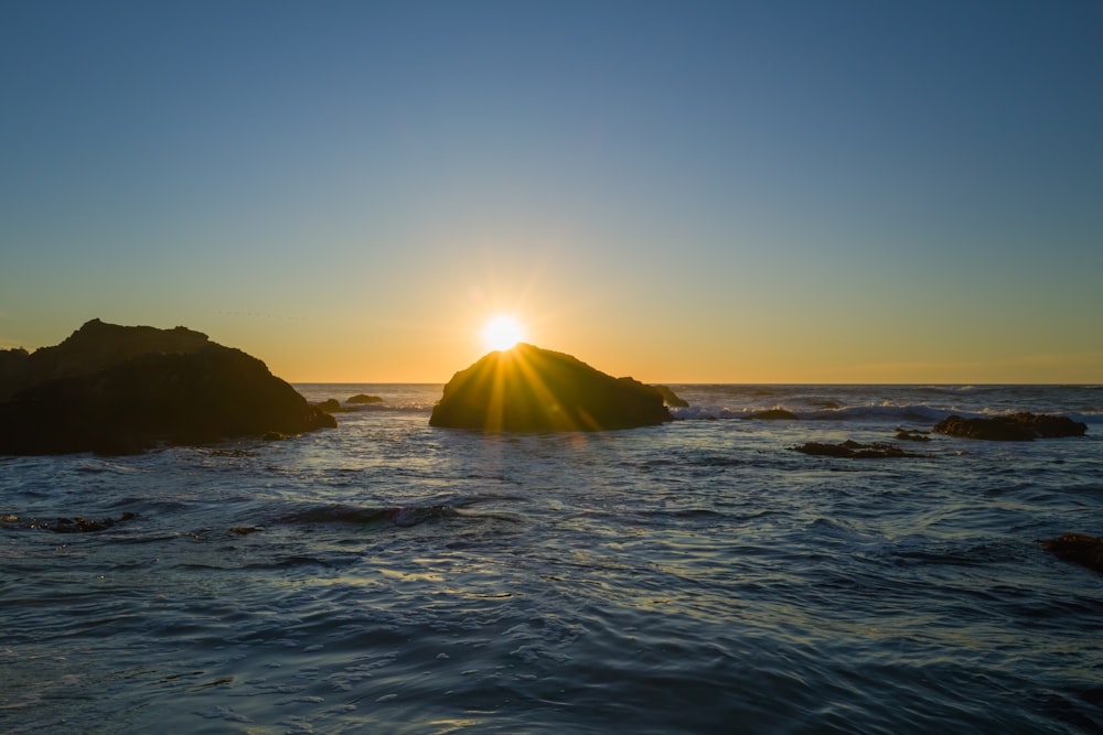 the sun setting over the ocean with rocks in the foreground