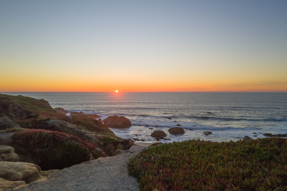 the sun is setting over the ocean with rocks