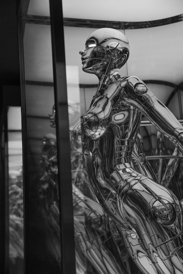 A highly detailed, reflective, and futuristic humanoid robot encased in a transparent display. The robot exhibits intricate metallic components and a sleek design, with an emphasis on mechanical and anatomical features.
