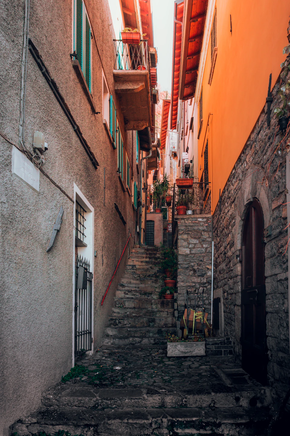 Narrow old stone street lined with potted plants and two colorful buildings in background
