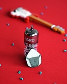 A vacuum tube labeled 'EGRO PC 86' sits upright on a red surface, surrounded by small, scattered blue beads. In the background, a blurred image of a small, toy-like guitar emphasizes the retro and musical theme. The triangular object in the front appears to be a stylized button or knob, complementing the overall vintage aesthetic.
