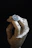 Close-up of a handcrafted guitar pick held between fingers with a dark, moody background.