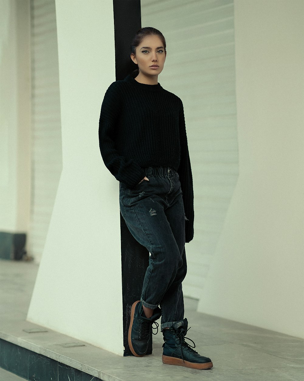 a woman leaning against a pillar in a black sweater and jeans