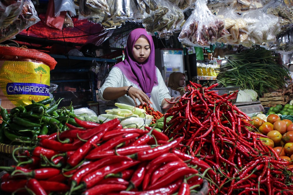 a woman standing in front of a pile of vegetables