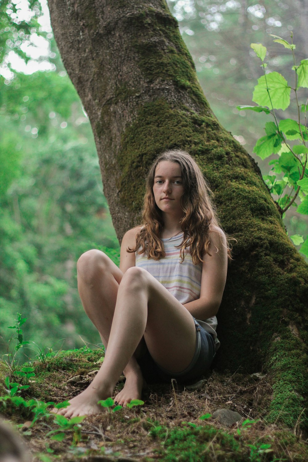 a young girl sitting on the ground next to a tree