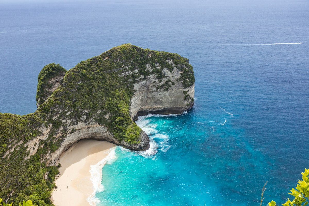 An aerial view of a beach with a rock formation in the water around Nusa Penida