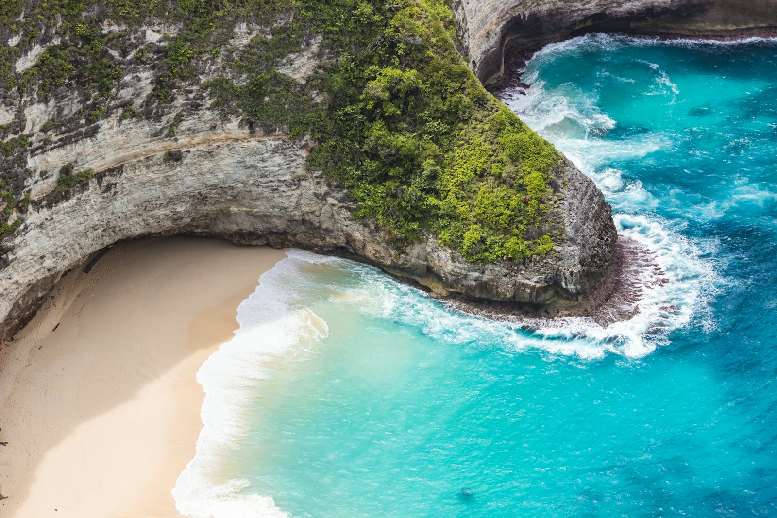 An aerial view of a sandy beach and a dramatic cliff in Nusa Penida, Bali