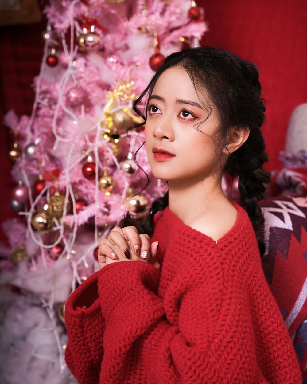 a woman in a red sweater standing in front of a christmas tree