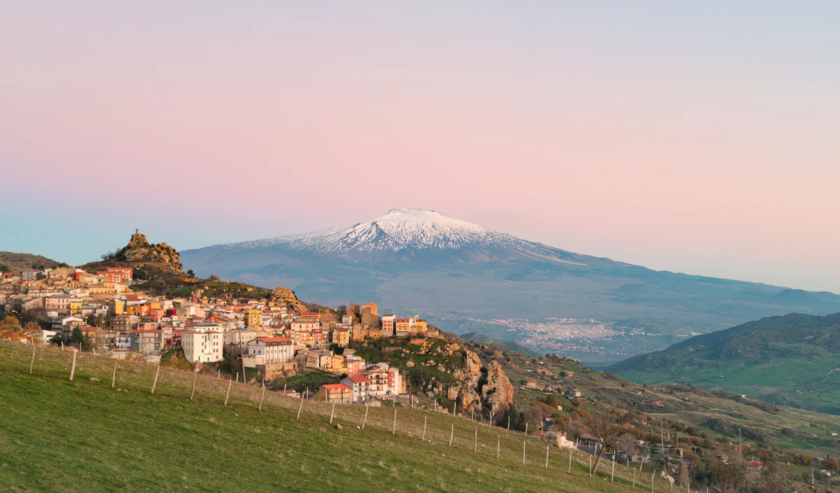 Sicilian village on a hillside with snow-capped Mount Etna behind
