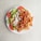 A white plate filled with a serving of doner kebab meat, fresh sliced tomatoes, cucumber, and lettuce, accompanied by creamy white and red sauces.