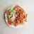 A white plate filled with a serving of doner kebab meat, fresh sliced tomatoes, cucumber, and lettuce, accompanied by creamy white and red sauces.